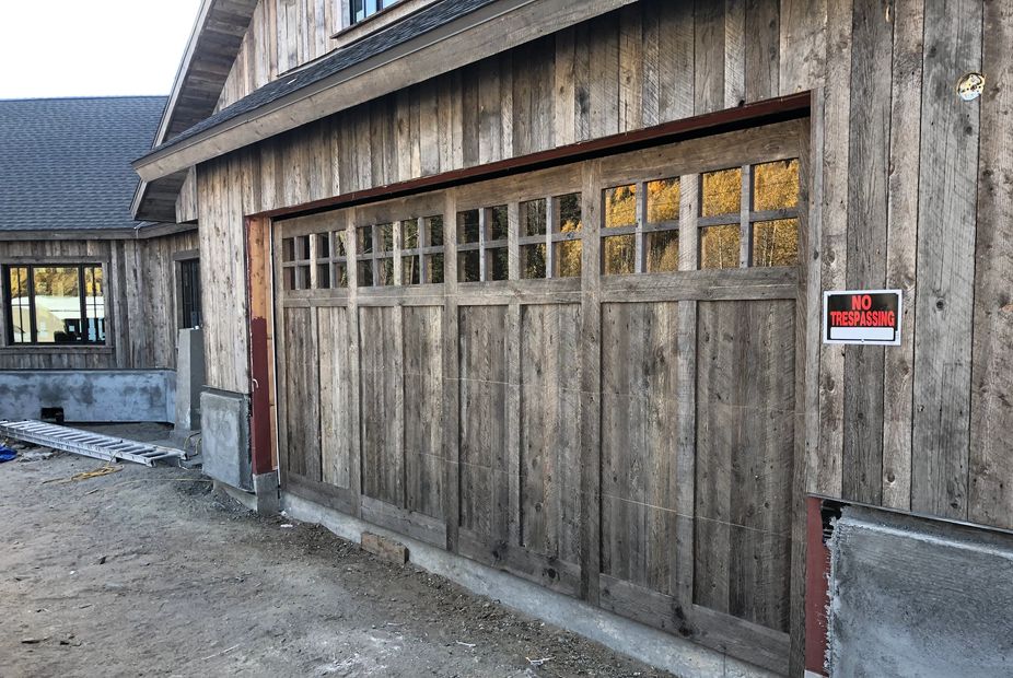 a wooden garage door with windows on top that blends in with the wooden home it's installed on