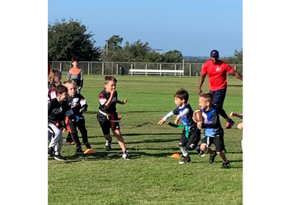 Kids playing flag football on a sunny field.