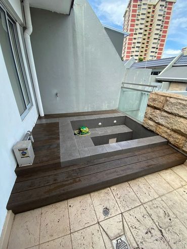 Small tiled jacuzzi or spa area on a balcony with city view.