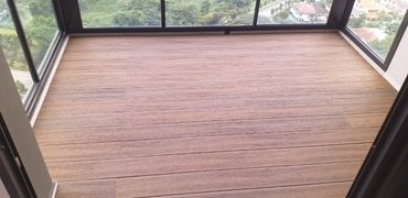 Empty balcony with wood-patterned flooring and glass railings overlooking greenery.