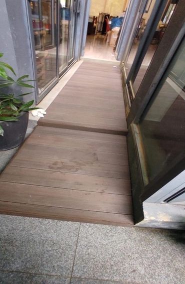 Wooden ramp between tiled floor and glass doors with a plant on the side.
