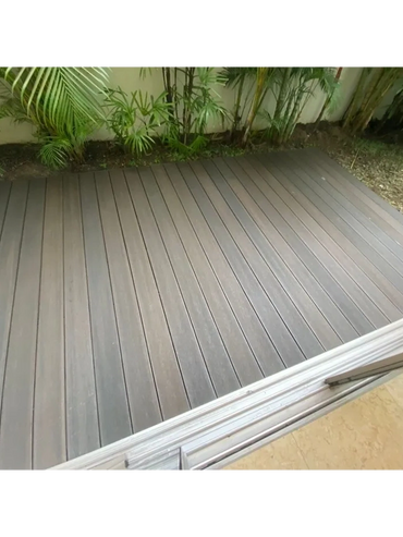 A clean outdoor deck with wooden planks and green plants along the wall.