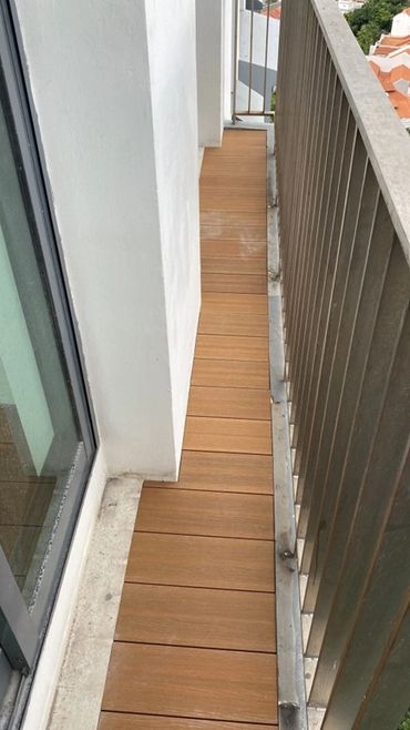 Narrow balcony with wooden flooring and metal railing.