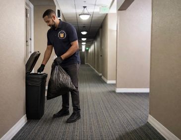 Man in uniform disposing of trash bag in a hallway trash bin.