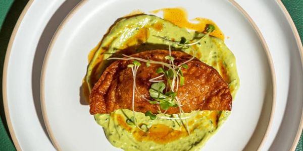Golden fried dumpling on creamy green sauce.