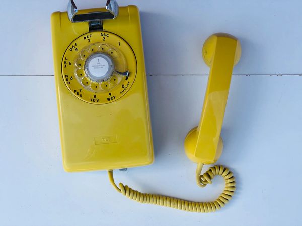 A wall mounted rotary dial phone made by Northern electric in 1988. Its a bright yellow color.