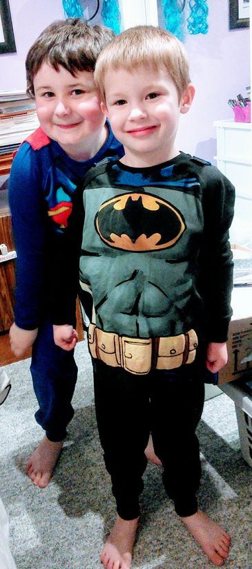 Katy's 2 young sons smiling and posing in front of camera in superhero pajamas.