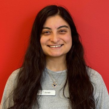A woman with long dark hair smiling against a red background.