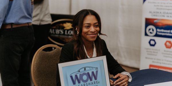 Smiling woman at a WOW EV Carshare booth during an event.