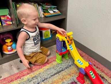 Child playing with toy cars and track during speech therapy session.