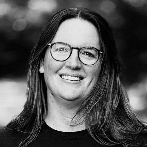 Smiling woman with glasses in a black sweater outdoors.