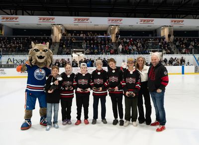 Youth hockey team posing on ice rink with mascot and adults.