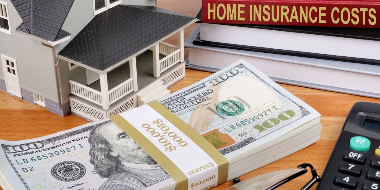 Model house, stack of $100 bills, insurance books, and calculator on desk.