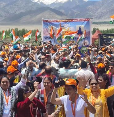 Crowd waving Indian flags at a vibrant outdoor event with mountains in the background.