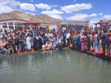 A large group gathers near water for a cultural or religious event under clear skies.
