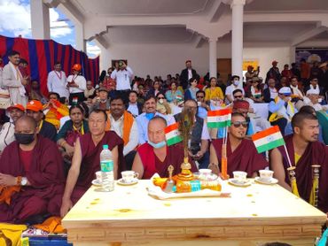 A gathering of monks and people seated at an event, with Indian flags displayed on the table.