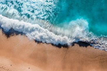 Aerial view of turquoise ocean waves crashing onto a sandy beach.
