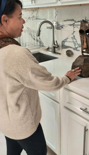 Woman touching a brown sculpture in a white kitchen.