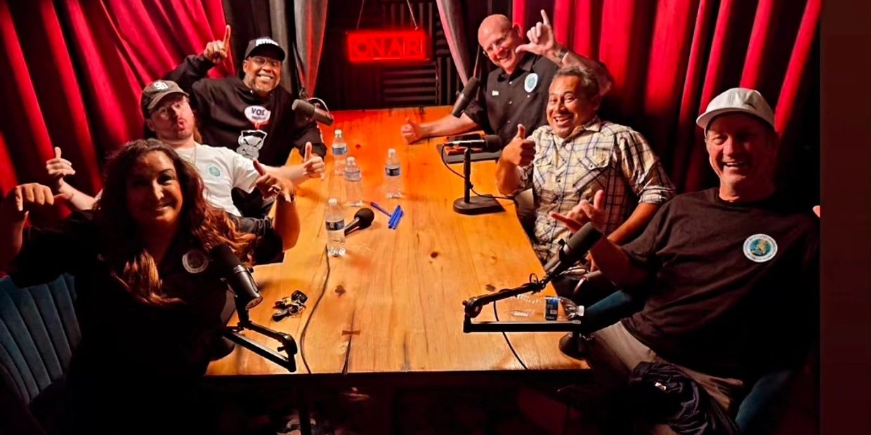 Group of people smiling and posing with thumbs up in a podcast studio.