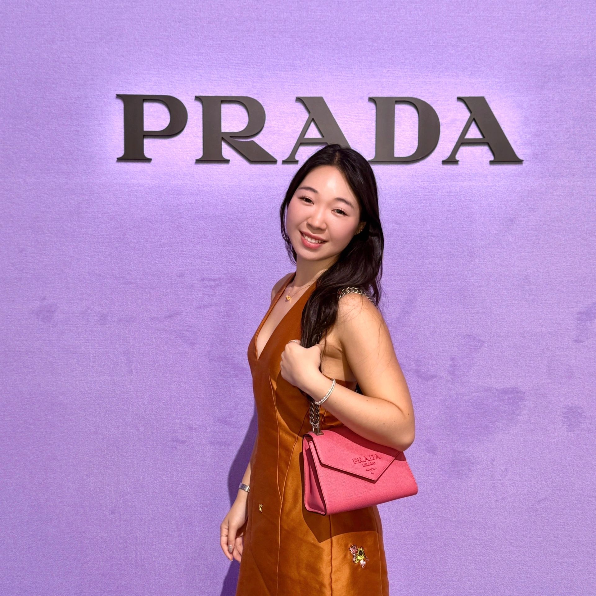 Young woman smiling in front of a purple Prada wall.
