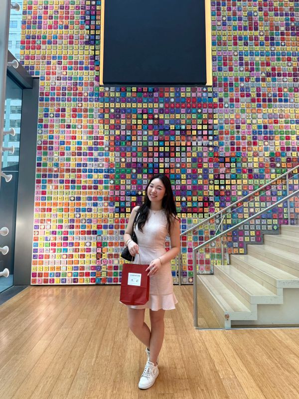 Woman standing in front of a colorful tiled wall inside a modern building.