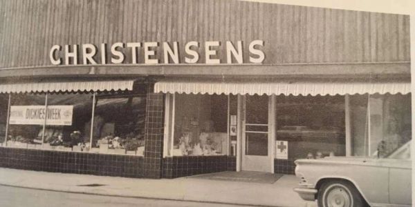 Black and white storefront of Christensens with a classic car.