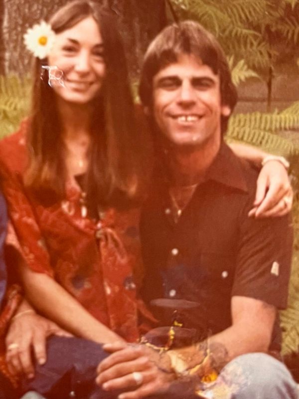 Smiling couple sitting together outdoors, woman with a flower in her hair.