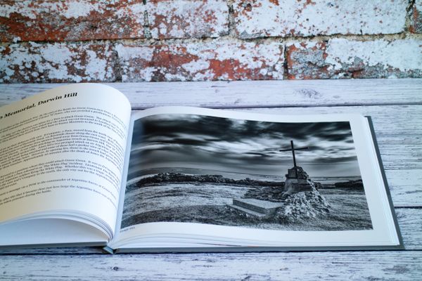 Open book displaying a black and white photo of a memorial with a cross on a stone mound.