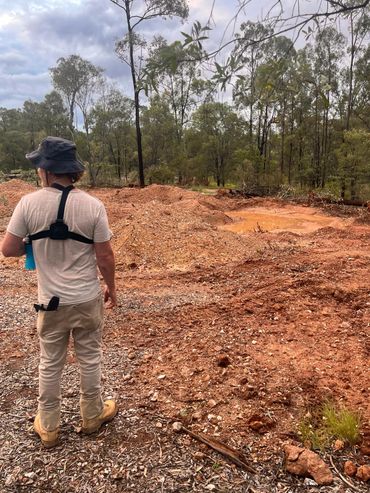 Man in outdoor gear stands on rocky terrain with trees in the background.