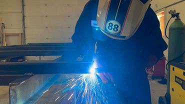 Welder in protective gear sparks bright light while working on metal.