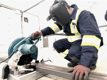 Worker using a power saw to cut metal with safety gear on.