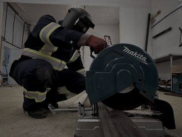 Worker using a Makita metal cutting saw with safety gear in an industrial setting.