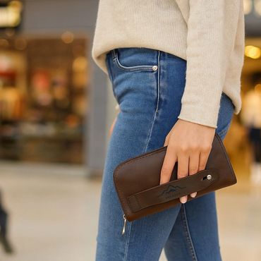 Person holding a brown leather wallet while wearing blue jeans and a beige sweater.