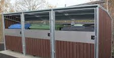 Three outdoor waste disposal bins with metal and wood paneling under a metal shelter.