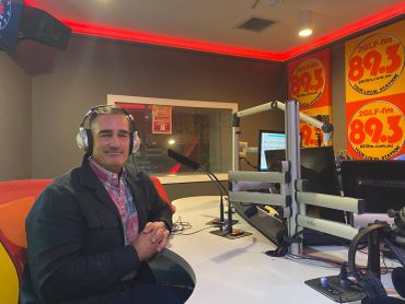 Man wearing headphones in a radio studio with 89.3 FM posters.