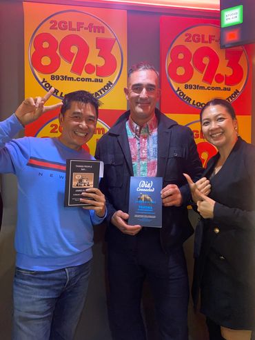 Three people smiling in a radio station holding books by James Elliott.
