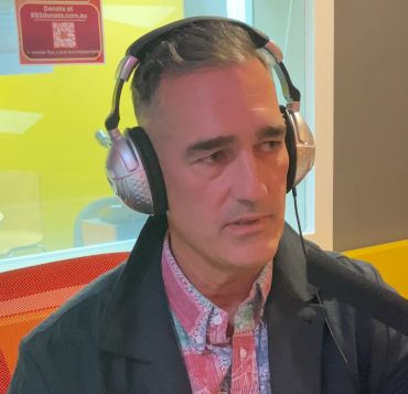 Man wearing headphones and a colorful shirt, sitting in an indoor setting.