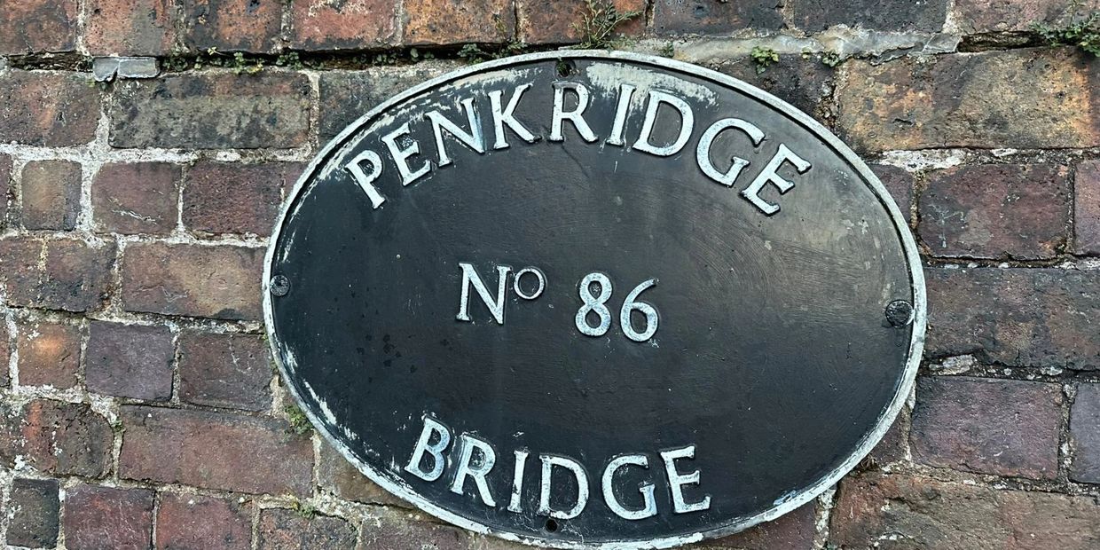 Oval plaque reading 'PENKRIDGE No 86 BRIDGE' on brick wall.