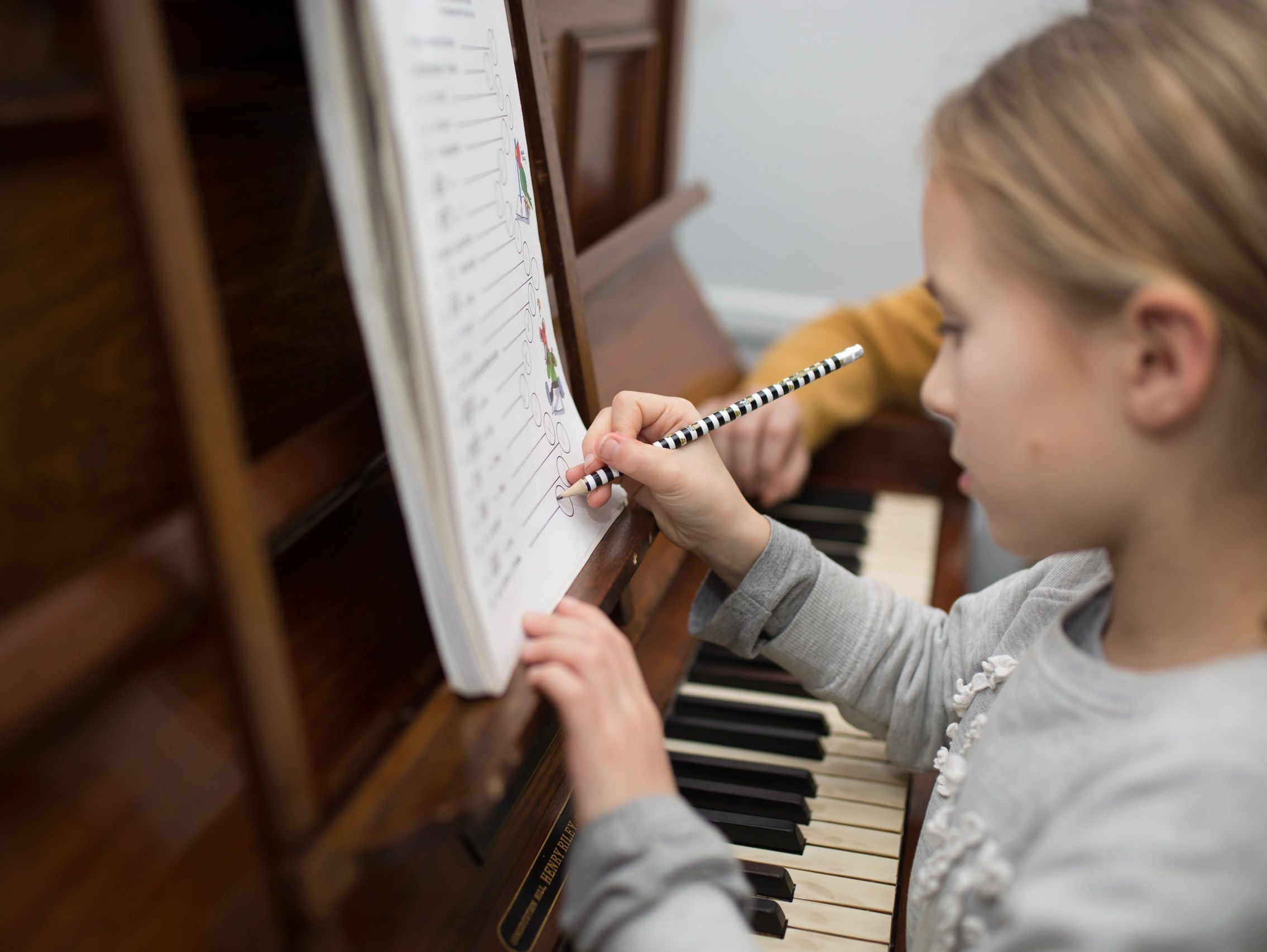 Child writing on a sheet placed on a piano while holding a pencil.