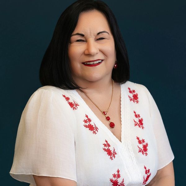 Smiling woman in white blouse with red floral embroidery.