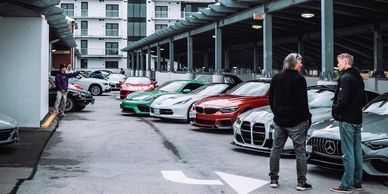Two men talk near a row of luxury cars in a parking garage.