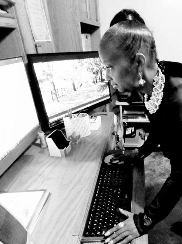 An elderly woman attentively looks at a computer screen in a home office.