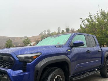 Blue Toyota Tacoma pickup truck parked on a wet road on a foggy day.