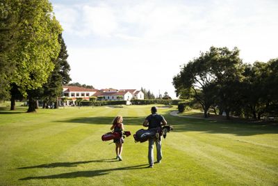 Man and girl walking toward clubhouse, carrying their clubs