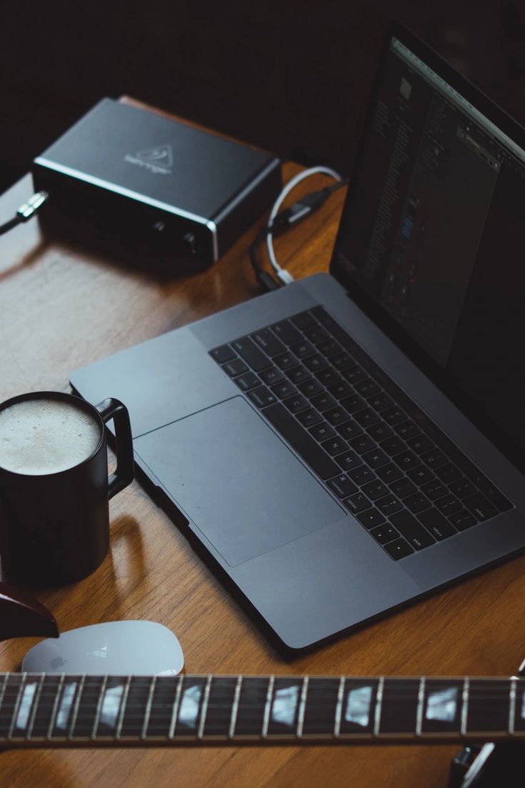 Image of guitar, laptop and cup on the table.