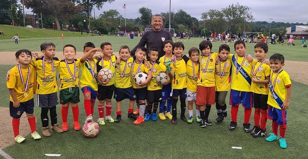 Youth soccer team with medals and coach on a sports field.