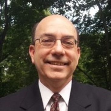 Smiling middle-aged man in glasses and suit outdoors.