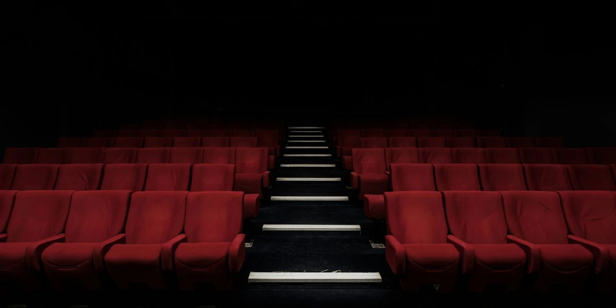 Empty red theater seats with central aisle lighting.