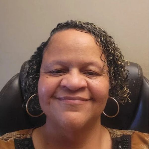 Woman with curly hair and hoop earrings smiling gently.