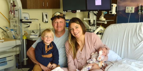 A happy family of four in a hospital room with a newborn baby.